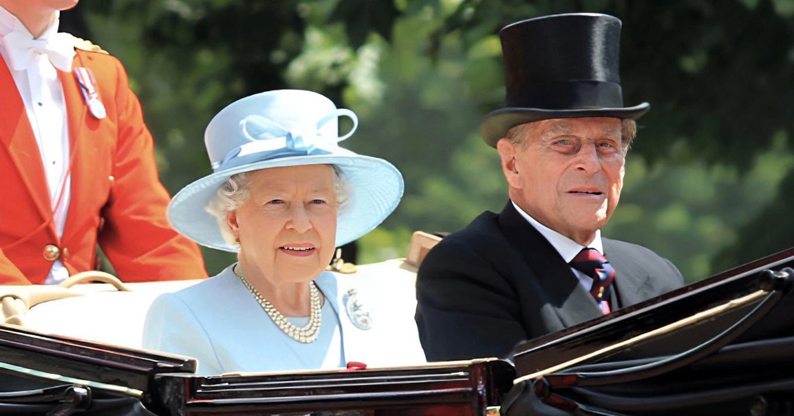 An elderly woman in a light blue outfit and hat sits beside an elderly man in a black suit and top hat in an open carriage, with another person in a red coat partially visible behind them. Trees are in the blurred background. An elderly woman in a light blue outfit and hat sits beside an elderly man in a black suit and top hat in an open carriage, with another person in a red coat partially visible behind them. Trees are in the blurred background.