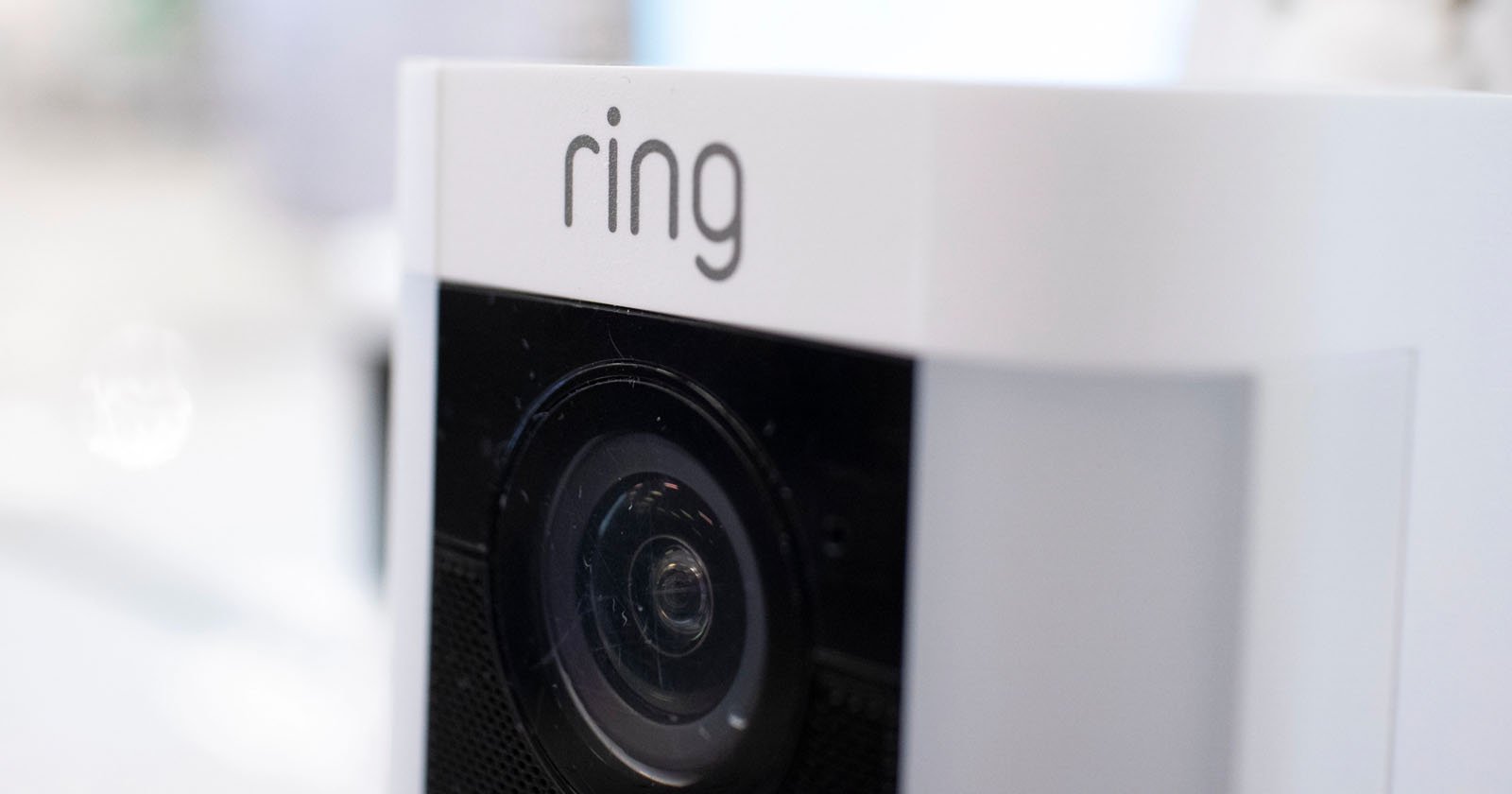 Close-up of a white Ring security camera showing the lens and the ring logo at the top. The background is blurred. Close-up of a white Ring security camera showing the lens and the ring logo at the top. The background is blurred.
