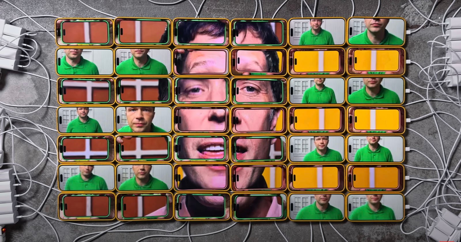 A collage of smartphone screens displays a man's face across multiple devices. Each screen shows a different part of the image, forming a complete face when viewed together. The phones are arranged in a grid, with chargers plugged in. A collage of smartphone screens displays a man's face across multiple devices. Each screen shows a different part of the image, forming a complete face when viewed together. The phones are arranged in a grid, with chargers plugged in.