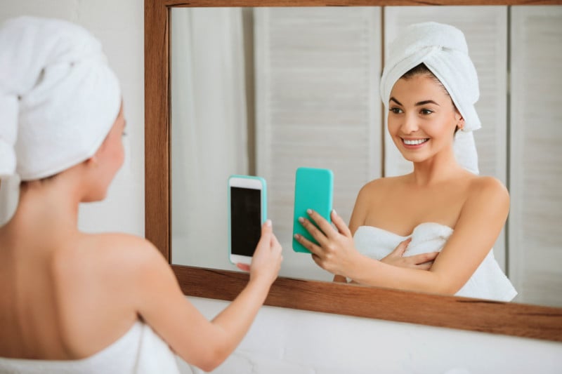beautiful happy woman in towel taking selfie in front of mirror in the bathroom