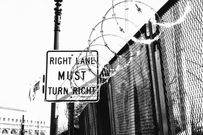 A photo of a street sign behind a barbed wire fence