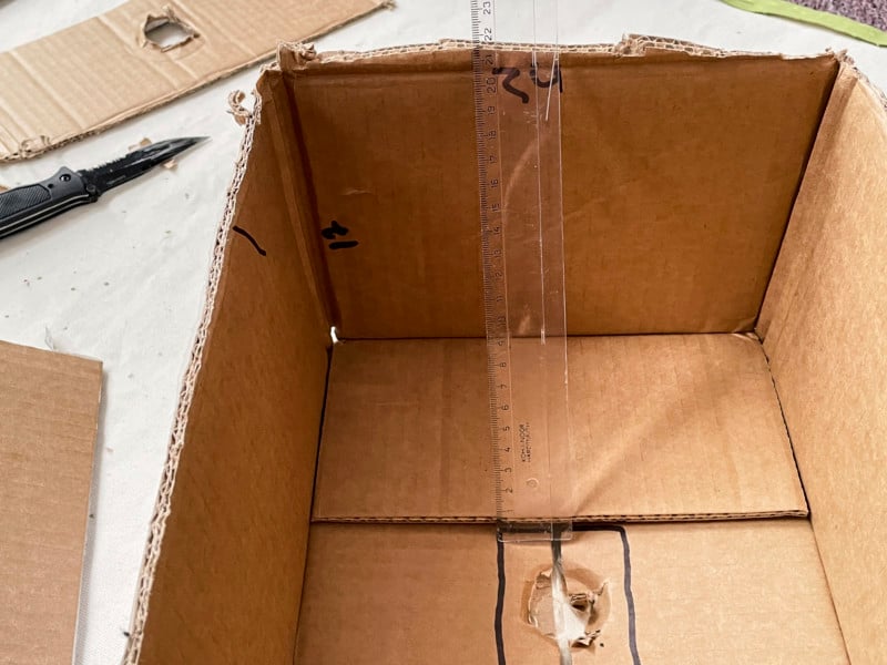 Using a ruler to measure the dimensions of a cardboard box to turn it into a DIY softbox