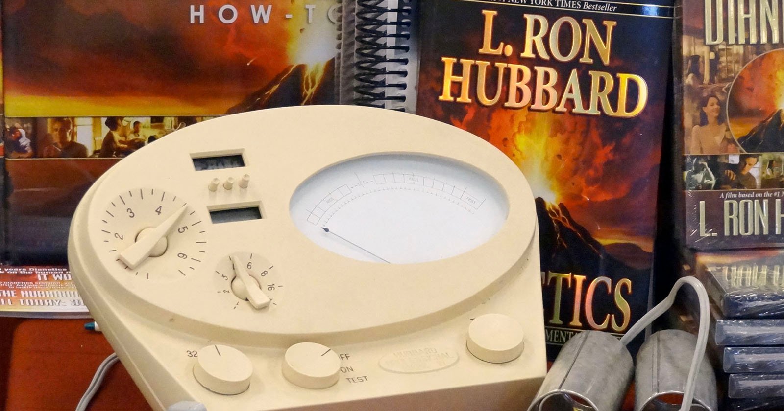 An E-Meter is seen in front of books by L. Ron Hubbard.