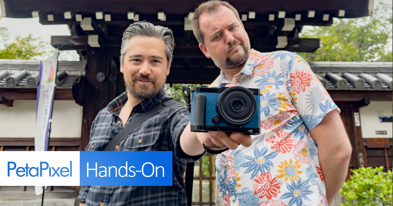 Two men are standing in front of a traditional Japanese building. One man holds a blue camera towards the viewer. The PetaPixel logo and the text Hands-On are displayed in the bottom left corner. Two men are standing in front of a traditional Japanese building. One man holds a blue camera towards the viewer. The PetaPixel logo and the text Hands-On are displayed in the bottom left corner.