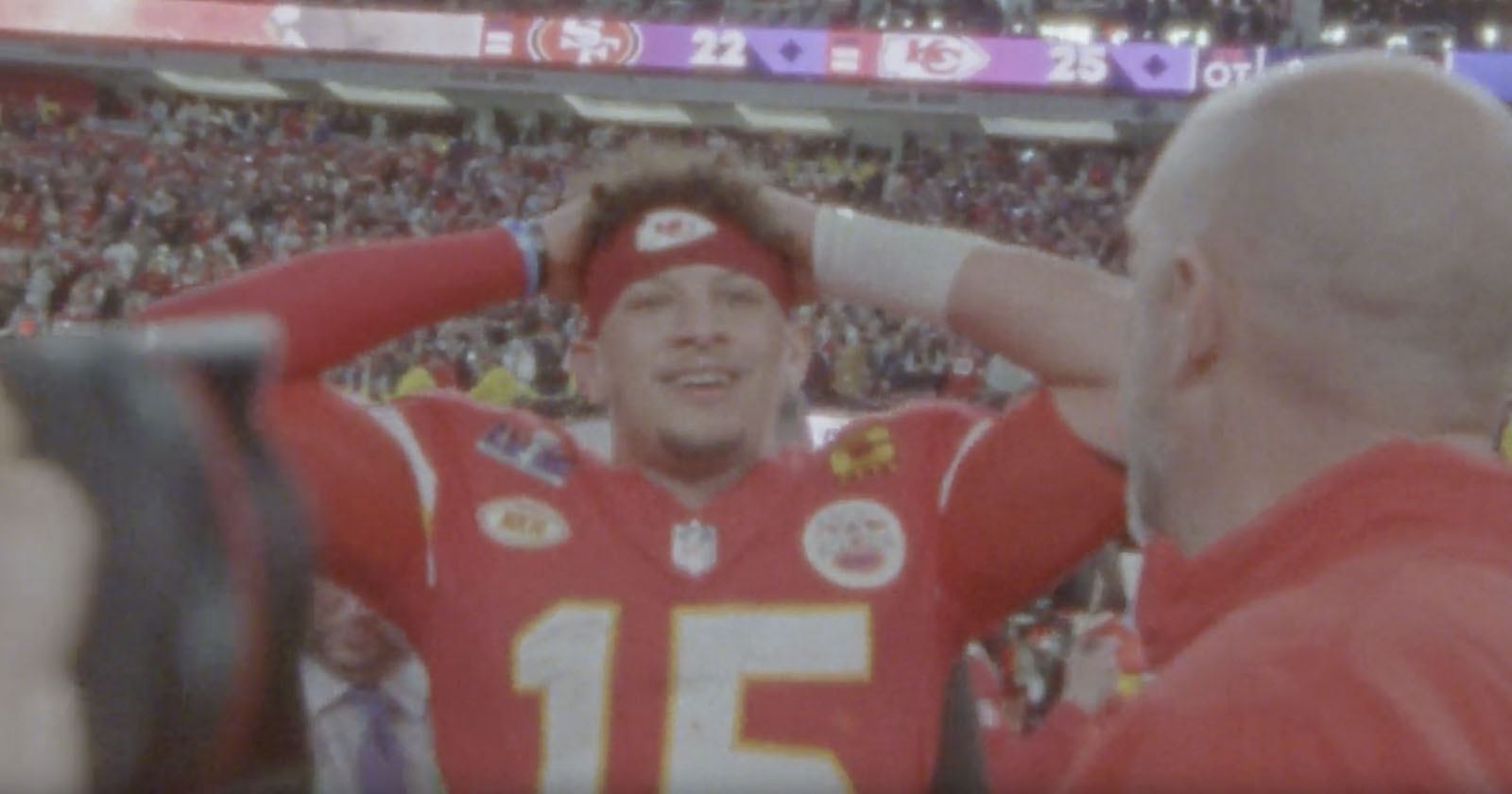 Patrick Mahomes wearing a red jersey with the number 15, and a red headband, looks joyful with his hands on his head amid a crowd in a stadium. The scoreboard in the background shows the 49ers 22 and Chiefs 25, suggesting a victory celebration. Patrick Mahomes wearing a red jersey with the number 15, and a red headband, looks joyful with his hands on his head amid a crowd in a stadium. The scoreboard in the background shows the 49ers 22 and Chiefs 25, suggesting a victory celebration.