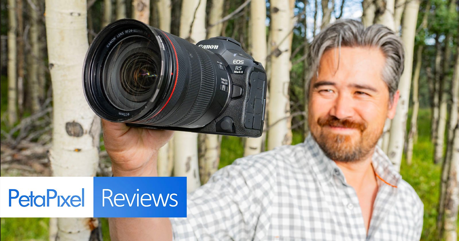 A person with gray hair and a beard holds up a Canon EOS R5 camera against a background of trees. The photo includes a PetaPixel Reviews logo in the bottom left corner. A person with gray hair and a beard holds up a Canon EOS R5 camera against a background of trees. The photo includes a PetaPixel Reviews logo in the bottom left corner.