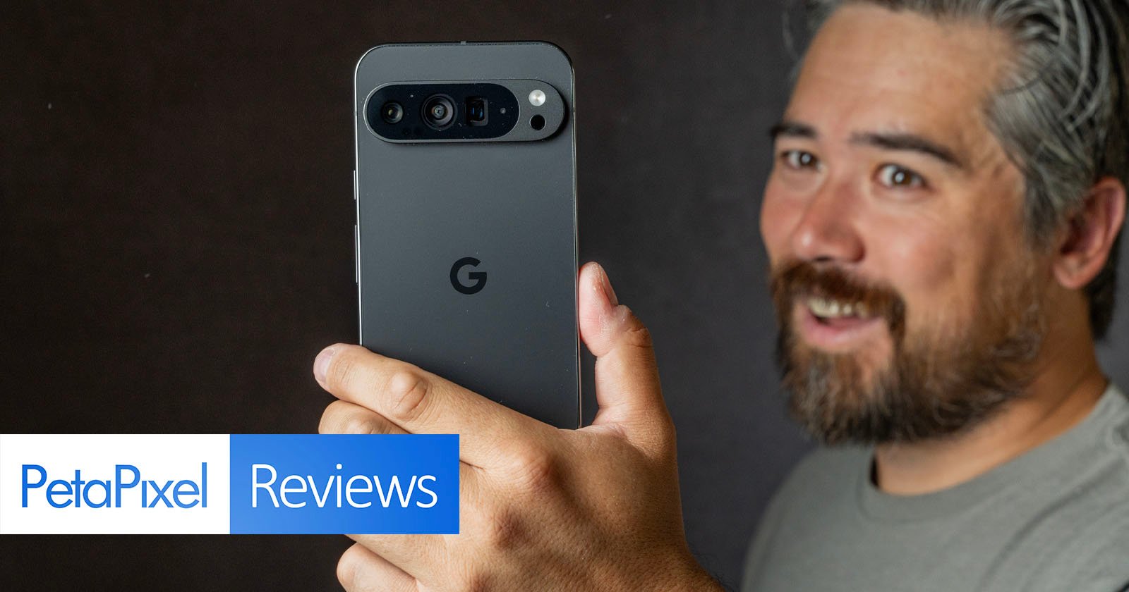 A person holds up a Google Pixel smartphone facing the camera. The phone's camera array is visible. The person has a beard, mustache, and gray hair. PetaPixel Reviews is prominently displayed in text on the left side of the image. A person holds up a Google Pixel smartphone facing the camera. The phone's camera array is visible. The person has a beard, mustache, and gray hair. PetaPixel Reviews is prominently displayed in text on the left side of the image.