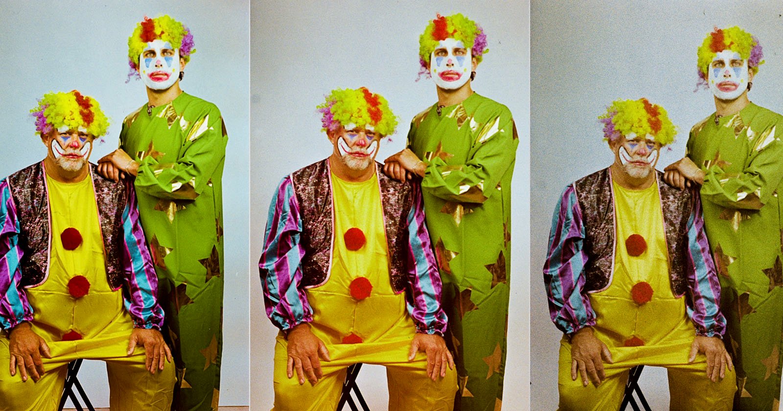 Two people are dressed as clowns in this image. The seated clown wears a yellow outfit with a multicolored vest and red buttons, while the standing clown wears a green suit with star patterns. Both have colorful wigs and face paint. Two people are dressed as clowns in this image. The seated clown wears a yellow outfit with a multicolored vest and red buttons, while the standing clown wears a green suit with star patterns. Both have colorful wigs and face paint.