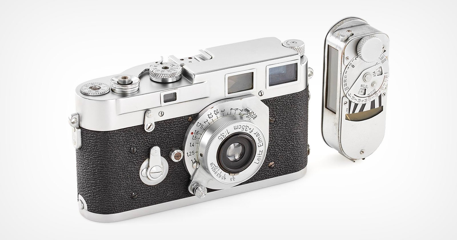 A vintage 35mm rangefinder camera with a black textured body and silver accents is shown. It's accompanied by a detachable light meter on the side. The camera has dials and a viewfinder on the top. A vintage 35mm rangefinder camera with a black textured body and silver accents is shown. It's accompanied by a detachable light meter on the side. The camera has dials and a viewfinder on the top.