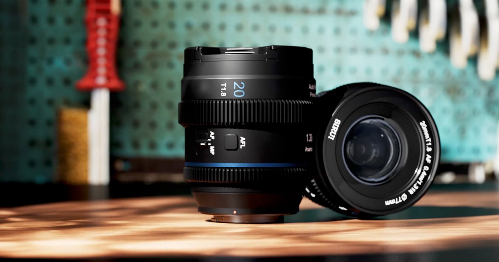 A camera lens with a 20mm focal length is placed upright on a wooden surface, with another lens lying beside it. The background has a blurred, teal pegboard with tools hanging on it. Warm sunlight casts soft shadows over the lenses. A camera lens with a 20mm focal length is placed upright on a wooden surface, with another lens lying beside it. The background has a blurred, teal pegboard with tools hanging on it. Warm sunlight casts soft shadows over the lenses.