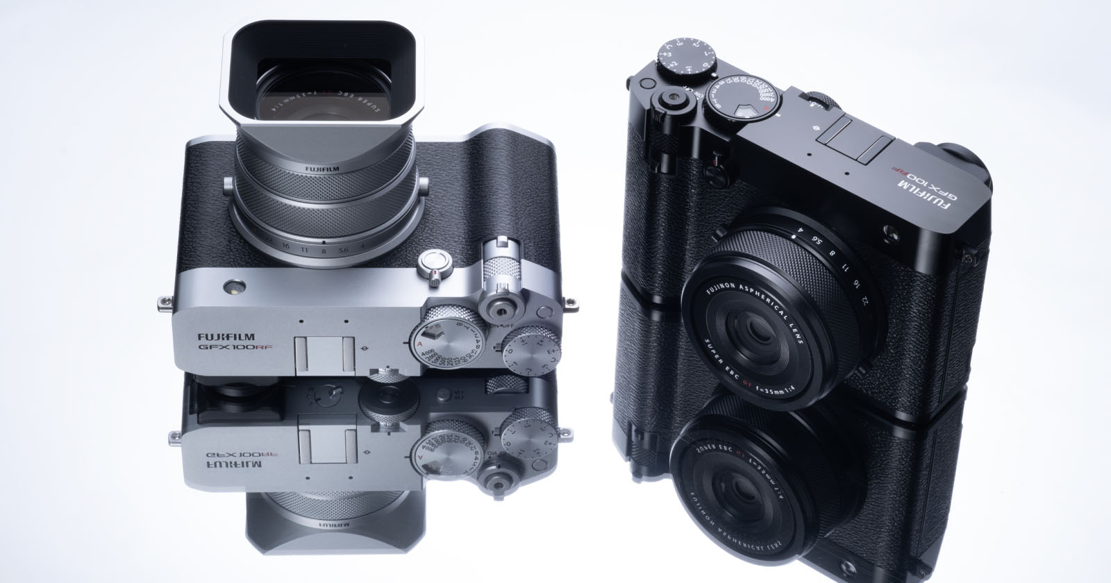 Two Fujifilm cameras are placed on a reflective surface. The camera on the left features a large lens and silver body, while the right camera is more compact with a black finish. Both are mirrored on the surface below them. Two Fujifilm cameras are placed on a reflective surface. The camera on the left features a large lens and silver body, while the right camera is more compact with a black finish. Both are mirrored on the surface below them.