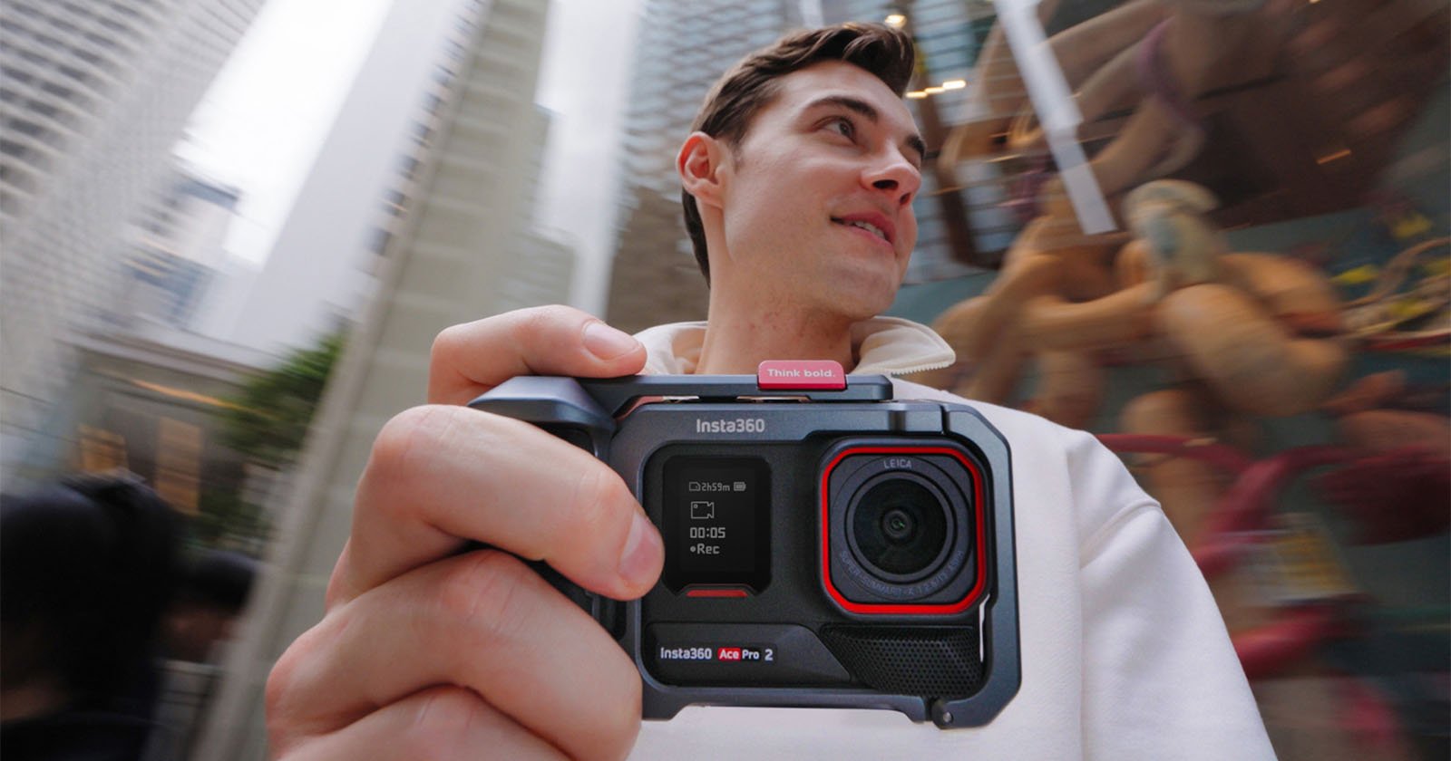 A person holding an Insta360 action camera, capturing a dynamic city scene. The background shows tall buildings and a blurred carousel. The person appears to be observing their surroundings with interest. A person holding an Insta360 action camera, capturing a dynamic city scene. The background shows tall buildings and a blurred carousel. The person appears to be observing their surroundings with interest.