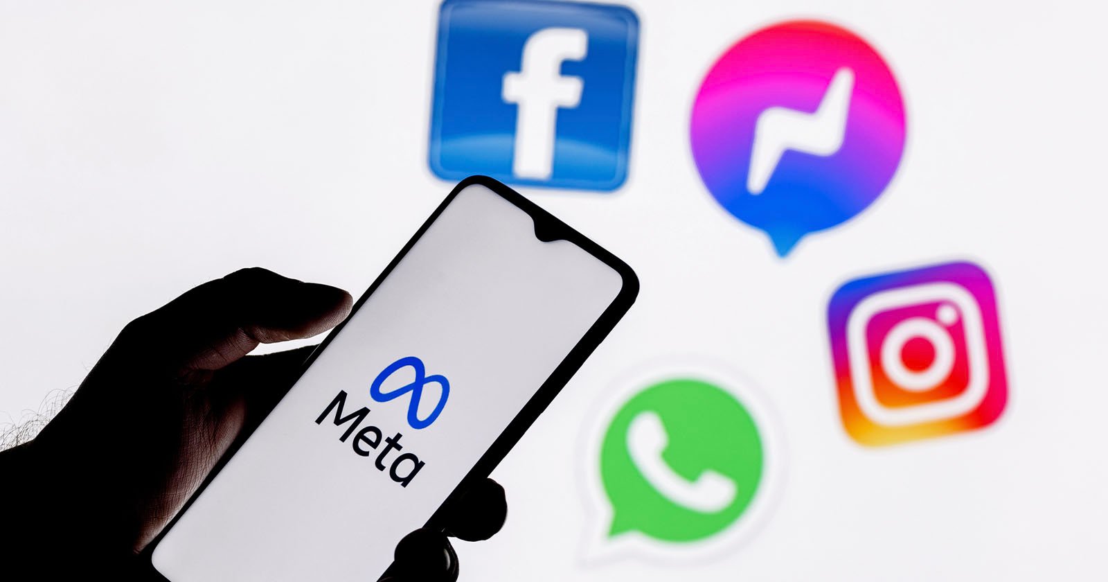 A person holds a smartphone displaying the Meta logo. In the background are social media app icons: Facebook, Messenger, Instagram, and WhatsApp, all associated with Meta. The image highlights Meta's branding and network of apps. A person holds a smartphone displaying the Meta logo. In the background are social media app icons: Facebook, Messenger, Instagram, and WhatsApp, all associated with Meta. The image highlights Meta's branding and network of apps.
