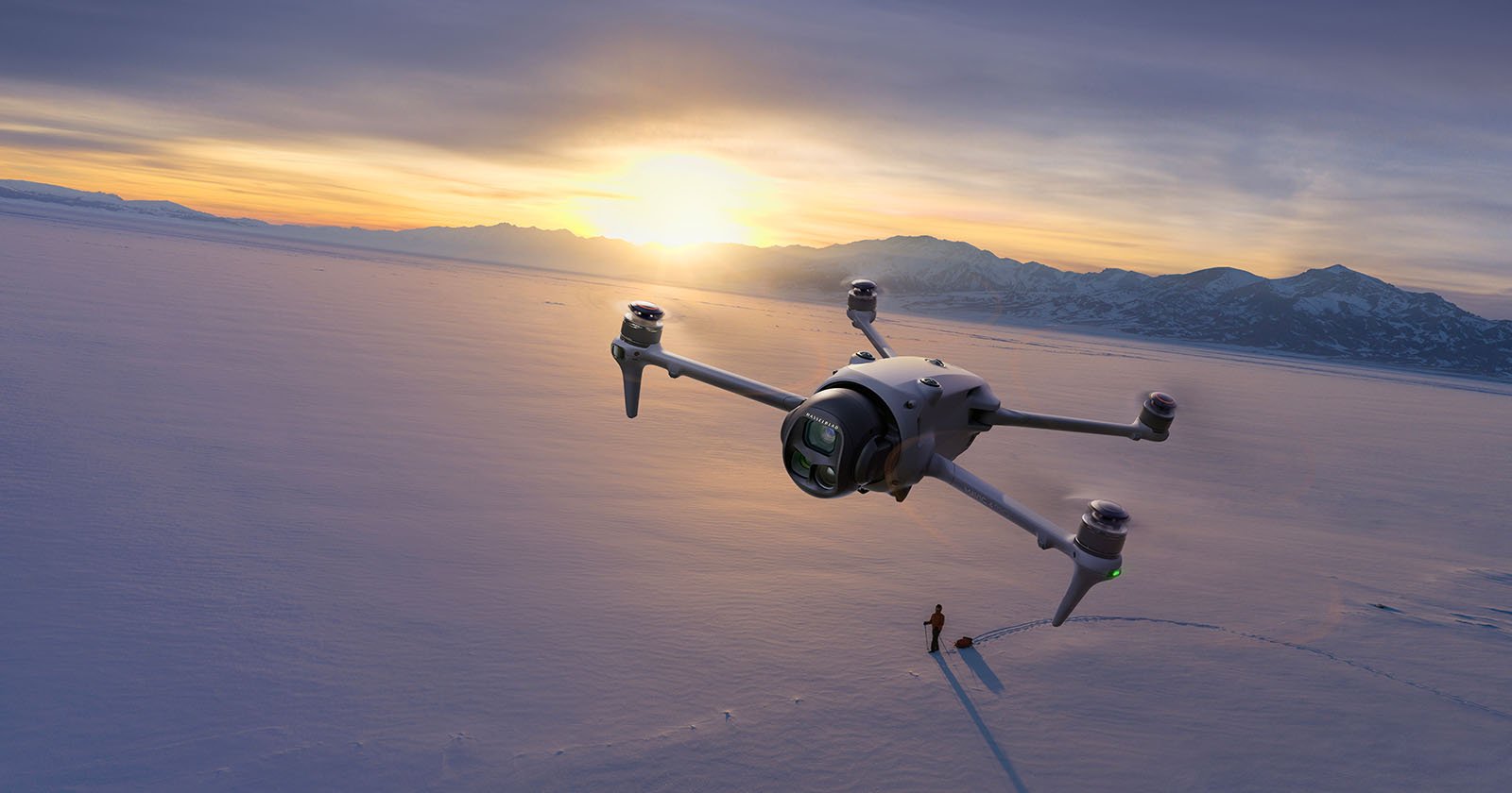 A large drone hovers over a snowy landscape at sunset, casting a shadow near a person standing on the snow with mountains visible in the background. A large drone hovers over a snowy landscape at sunset, casting a shadow near a person standing on the snow with mountains visible in the background.
