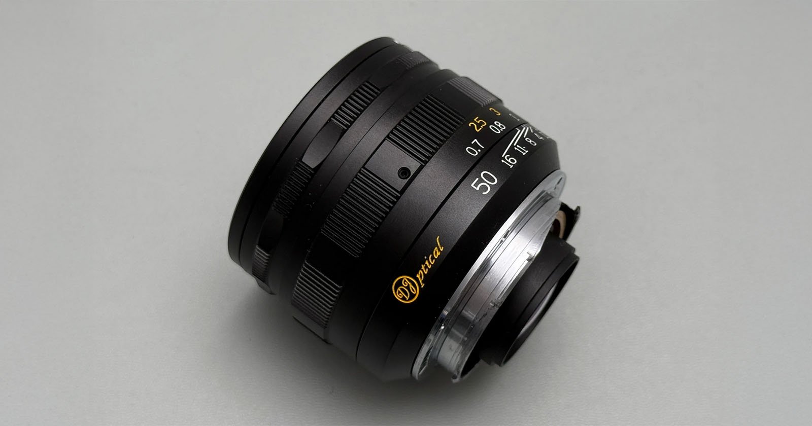 A close-up photo of a black camera lens with gold and white markings, including 50 for the focal length, set against a plain light gray background. A close-up photo of a black camera lens with gold and white markings, including 50 for the focal length, set against a plain light gray background.