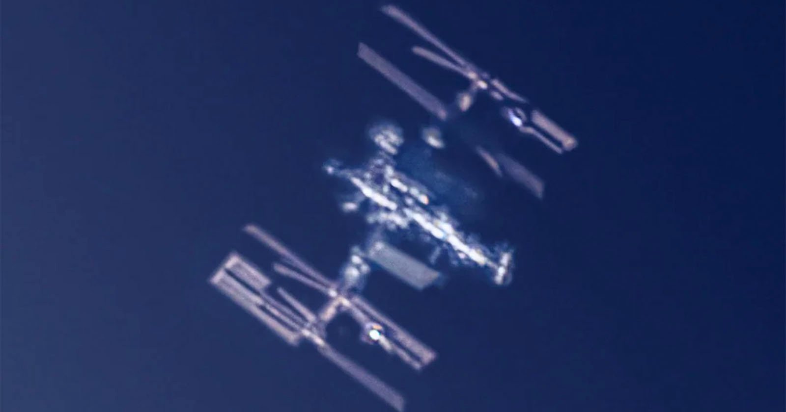 A blurred, close-up image of the International Space Station (ISS) orbiting against a dark blue sky, with its solar panels and structural modules visible. A blurred, close-up image of the International Space Station (ISS) orbiting against a dark blue sky, with its solar panels and structural modules visible.