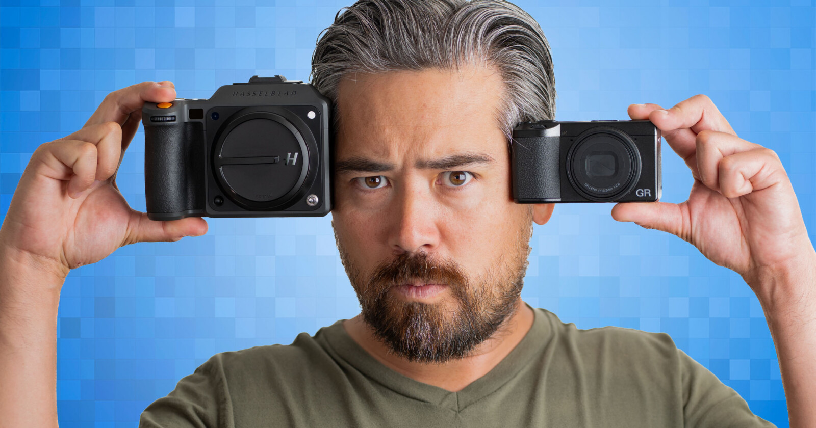 A man with gray hair and a beard holds two cameras up to his face, one in each hand, against a blue pixelated background. He looks directly at the camera with a serious expression. A man with gray hair and a beard holds two cameras up to his face, one in each hand, against a blue pixelated background. He looks directly at the camera with a serious expression.