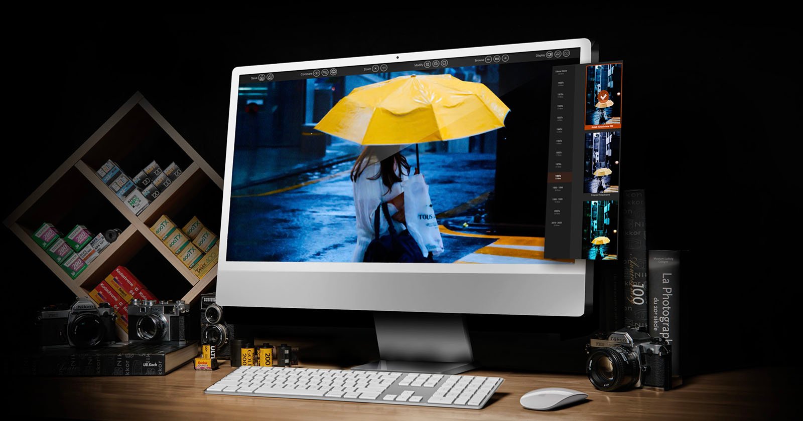 A desktop computer displays a photo of a person holding a yellow umbrella in the rain. Surrounding the monitor are film cameras, photo film rolls, photography books, and a shelf with film boxes, all set on a wooden desk. A desktop computer displays a photo of a person holding a yellow umbrella in the rain. Surrounding the monitor are film cameras, photo film rolls, photography books, and a shelf with film boxes, all set on a wooden desk.