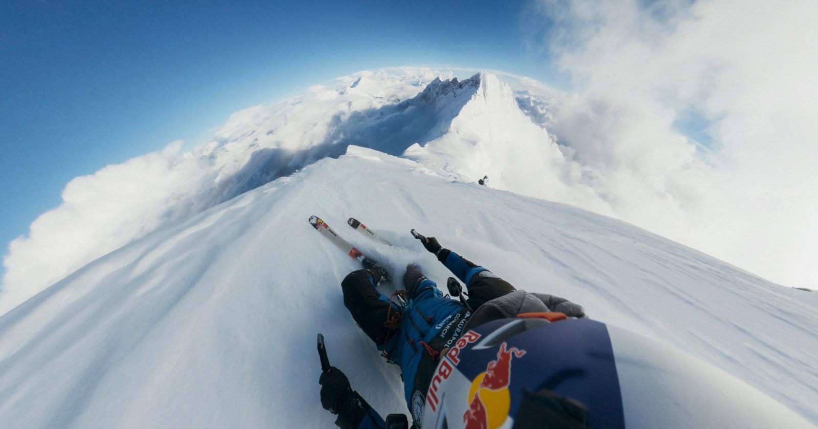 A skier in winter gear, seen from a first-person view, speeds down a narrow, snowy mountain ridge surrounded by clouds and distant peaks, creating a dramatic sense of height and adventure. A skier in winter gear, seen from a first-person view, speeds down a narrow, snowy mountain ridge surrounded by clouds and distant peaks, creating a dramatic sense of height and adventure.