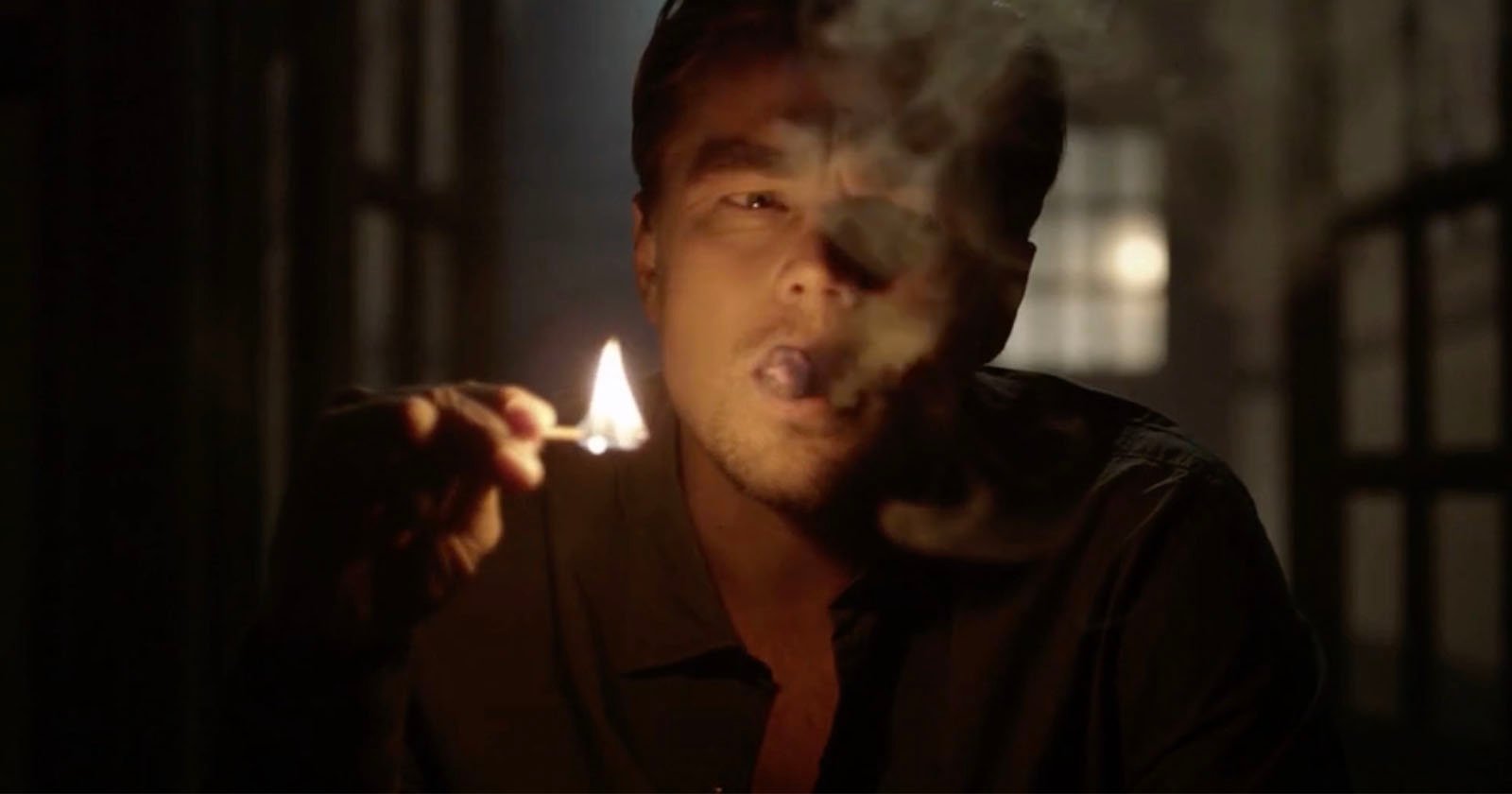 A man in a dimly lit room holds a lit match close to his face while smoking, with smoke partially obscuring his features. A man in a dimly lit room holds a lit match close to his face while smoking, with smoke partially obscuring his features.