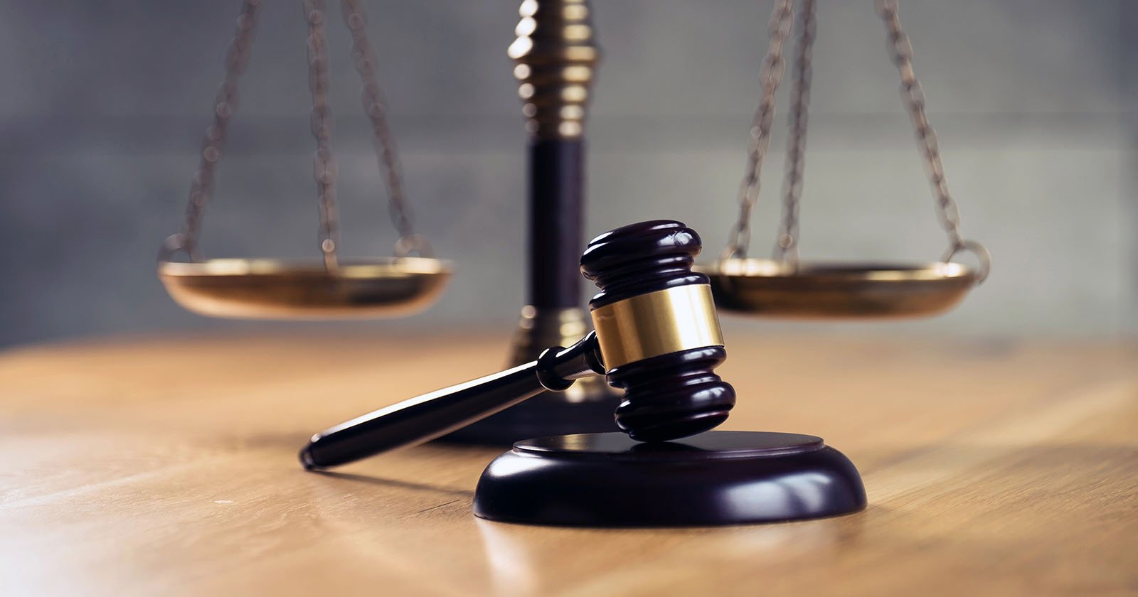 A wooden judge’s gavel rests on a sound block in front of a blurred brass balance scale, symbolizing law and justice on a wooden table. A wooden judge’s gavel rests on a sound block in front of a blurred brass balance scale, symbolizing law and justice on a wooden table.